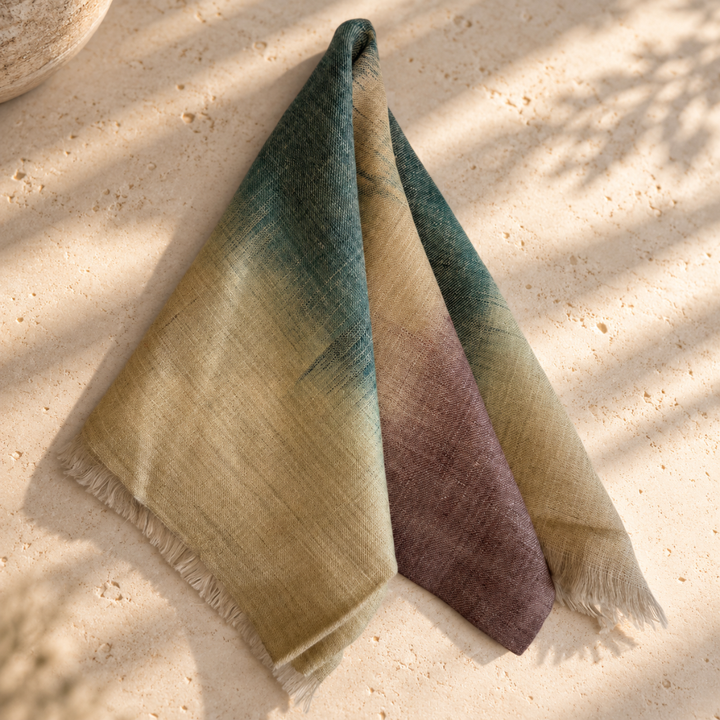 A lightweight pashmina handwoven scarf with fringed edges, folded to show its gradient color story. The color transitions from a deep teal-green at the top, through a warm beige/cream middle, to a muted plum-purple at the bottom.
