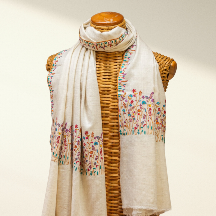 Beige pashmina scarf with floral embroidery on a wooden mannequin against a white background