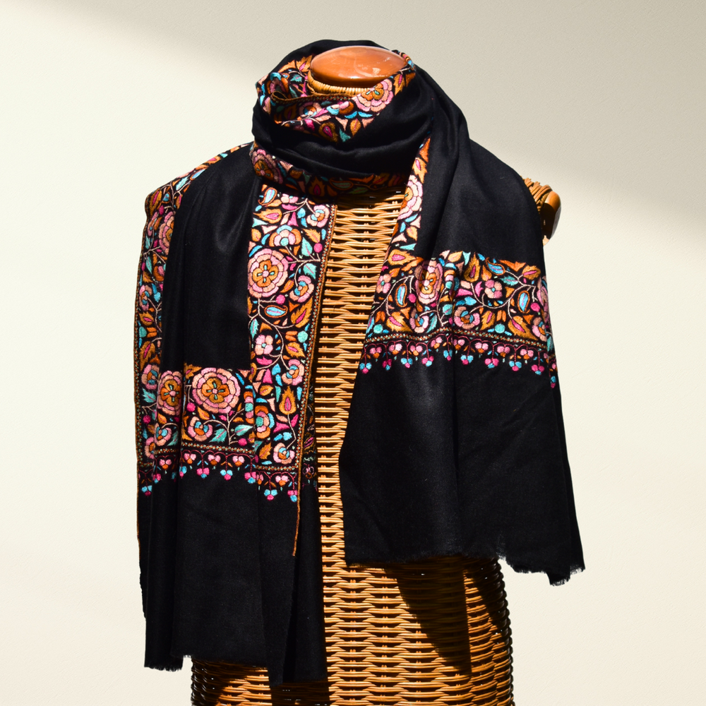 Black pashmina shawl with colorful floral patterns draped over a mannequin on a neutral background