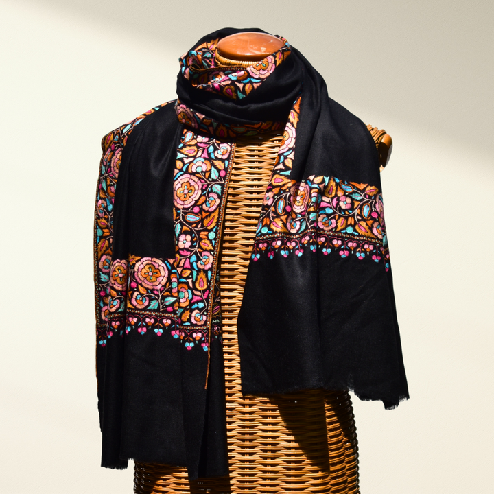 Black pashmina shawl with colorful floral patterns draped over a mannequin on a neutral background