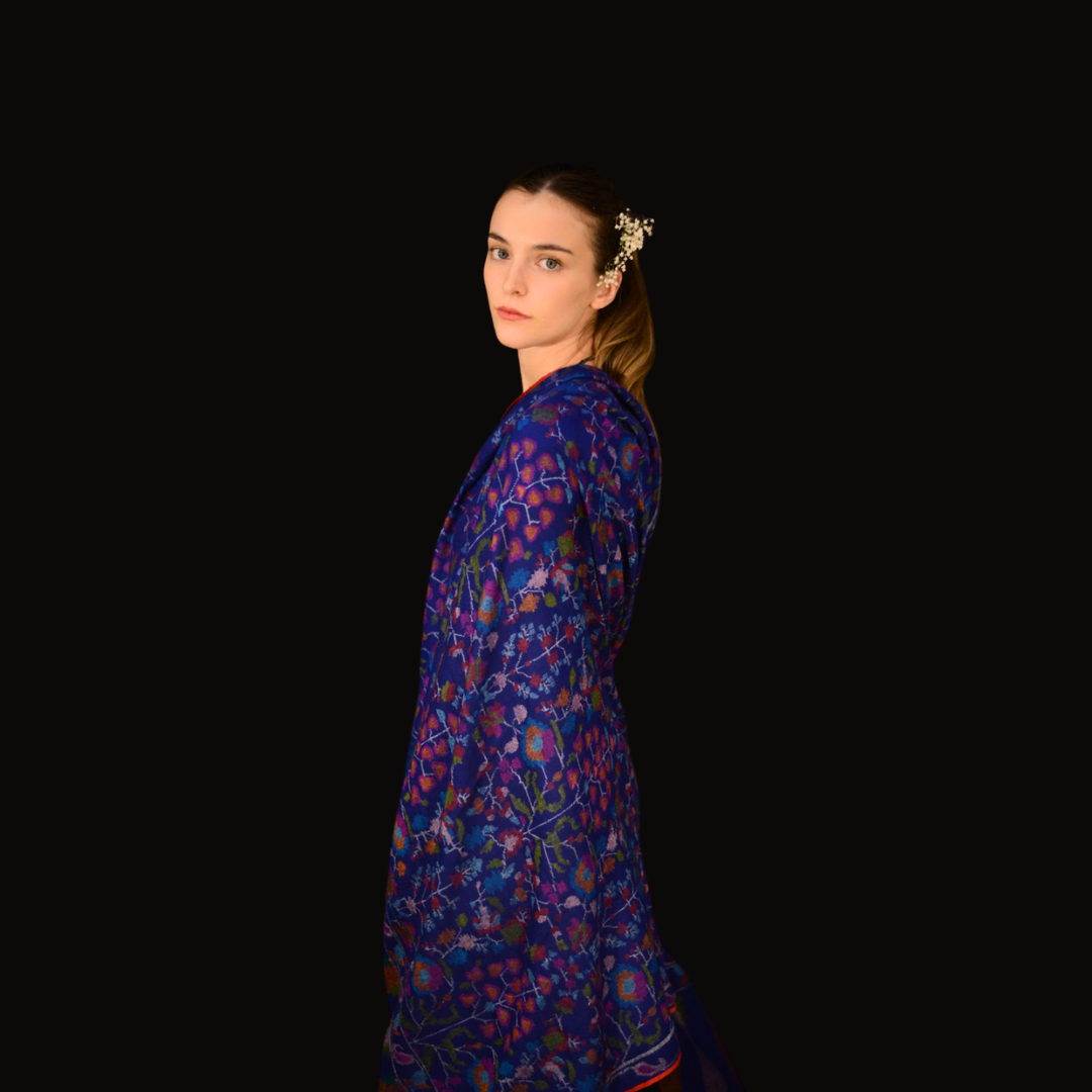Woman wearing a blue kani pashmina shawl against a black background
