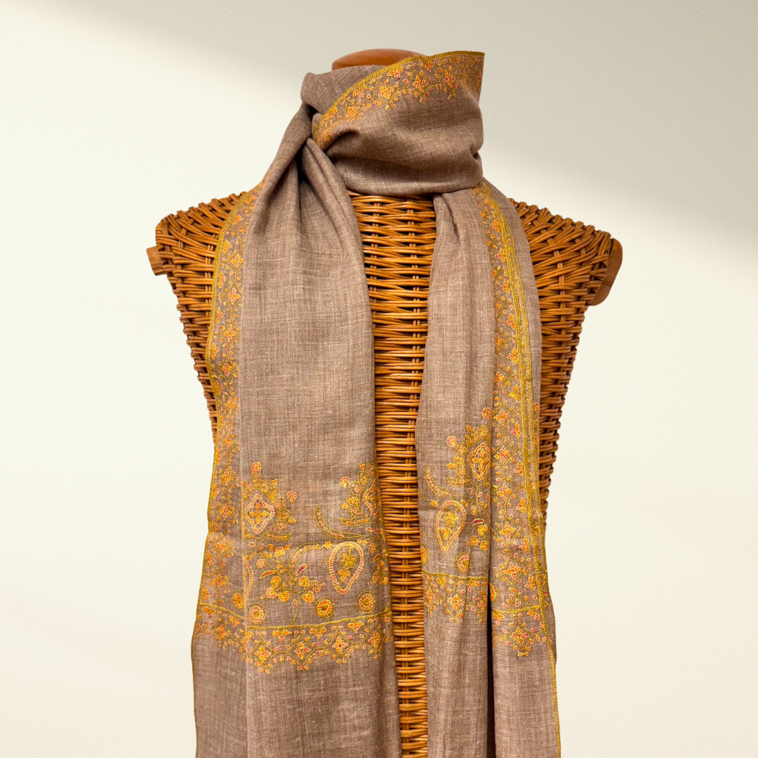 Brown scarf with yellow patterns draped over a wicker basket on a beige background
