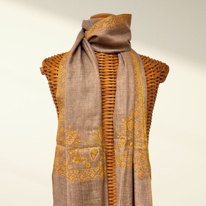 Brown scarf with yellow patterns draped over a wicker basket on a beige background