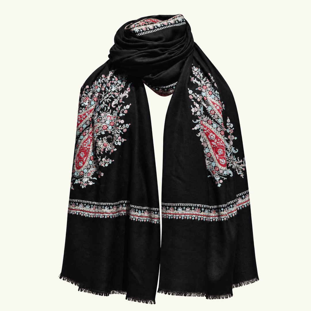 A black pashmina scarf with intricate red, pink, and white paisley and floral embroidery, draped elegantly against a light cream background.