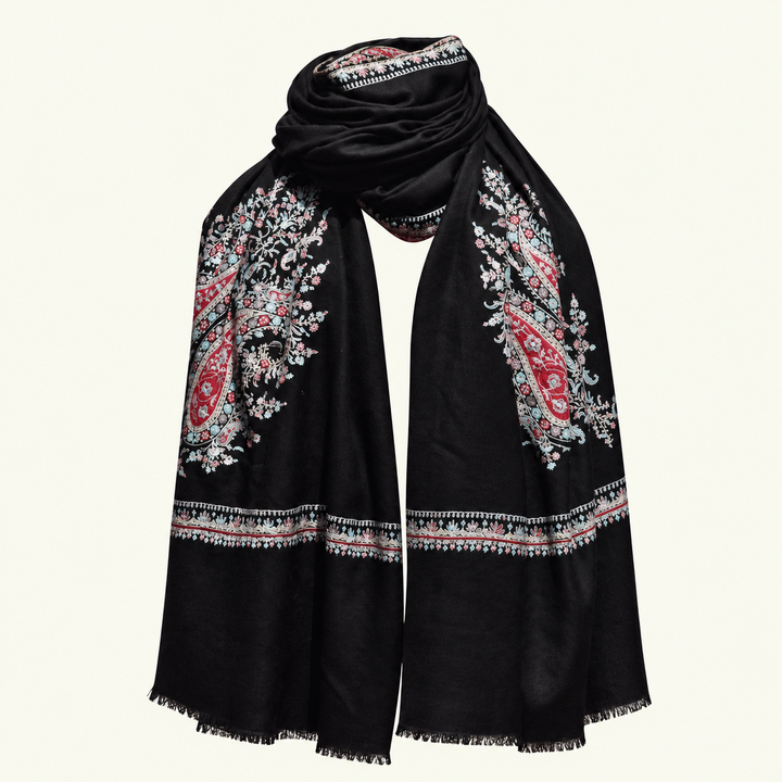 A black pashmina scarf with intricate red, pink, and white paisley and floral embroidery, draped elegantly against a light cream background.