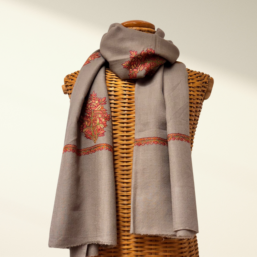 Gray pashmina scarf with floral embroidery draped over a wicker mannequin on a light background