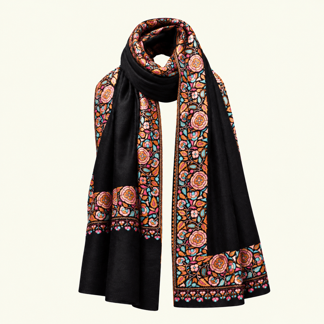 A black pashmina scarf with intricate multicolor floral and geometric patterns along the borders, displayed on a light cream background.