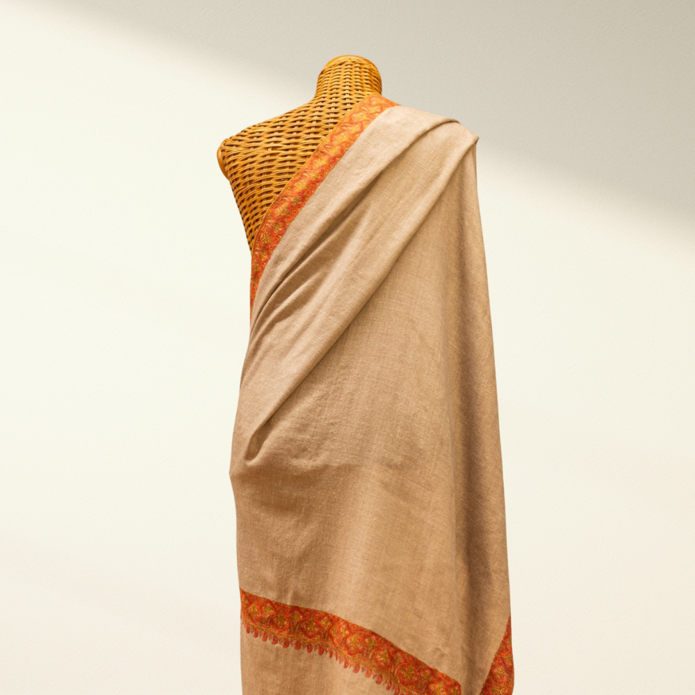 Mannequin wearing a beige pashmina shawl with orange accents on a plain background