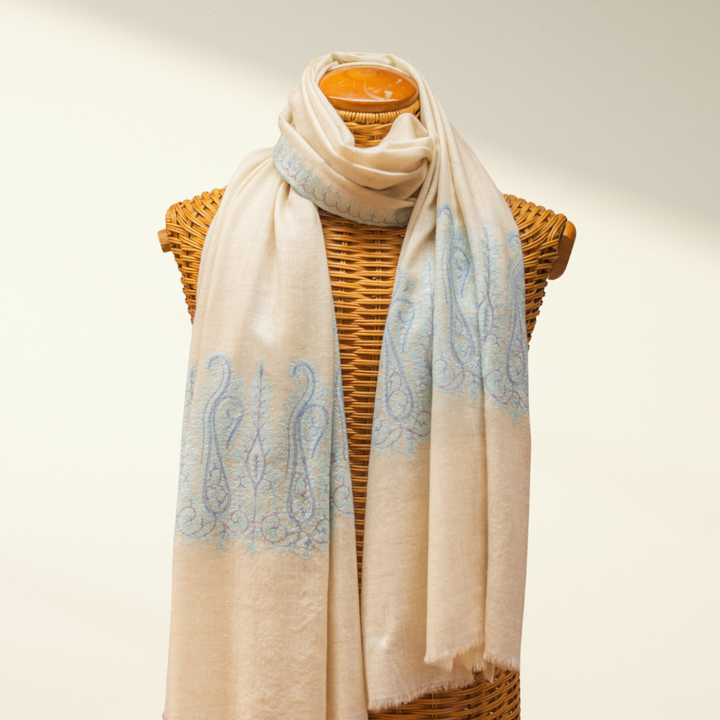 Pashmina scarf with blue patterns draped over a wicker basket on a neutral background