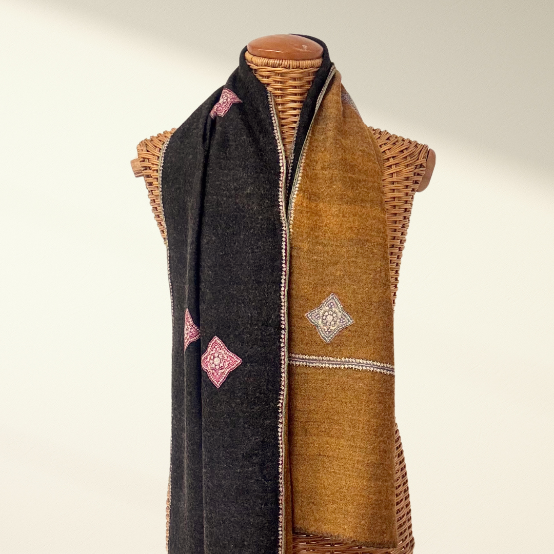 Reversible cashmere scarf , one side black and one side brown with embroidery, draped over a mannequin with a wicker mannequin