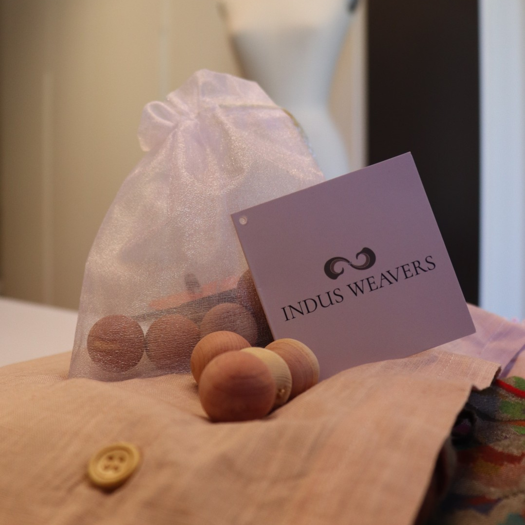 Indus Weavers pashmina with cedar balls and a drawstring bag on a wooden surface.