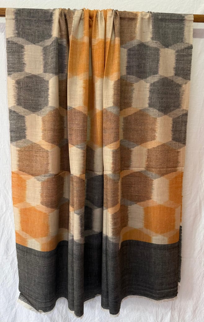 Geometric patterned pashmina with orange and brown colors on a wooden rod.