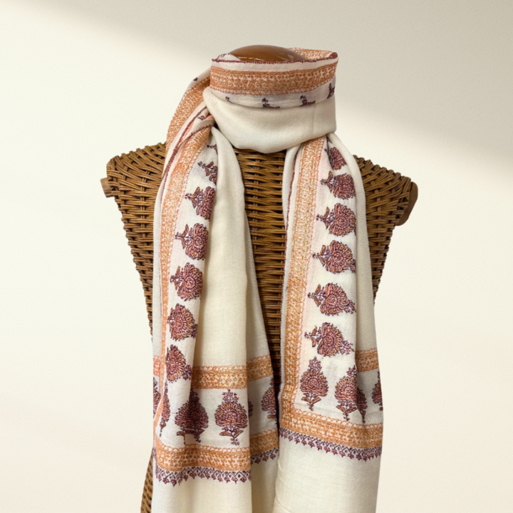 White Pashmina scarf with brown floral patterns draped over a wicker mannequin on a neutral background