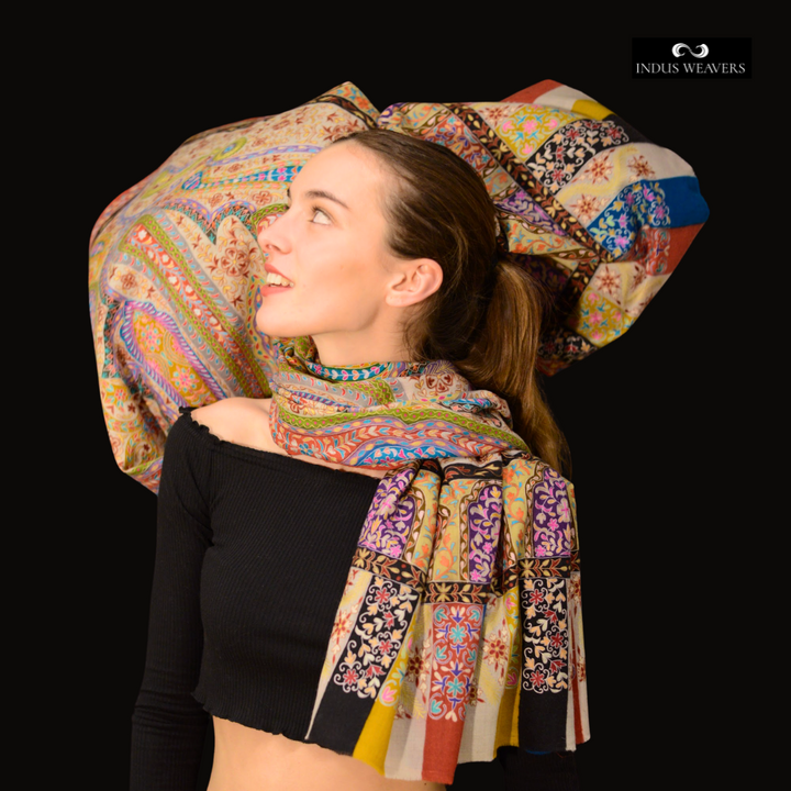 Woman wearing kalamkari Pashmina Shawl Victoria with a large decorative pillow in the background, featuring the brand 'Indus Weavers'.