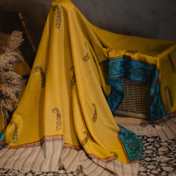 Yellow pashmina shawl with intricate patterns draped over a wicker chair.