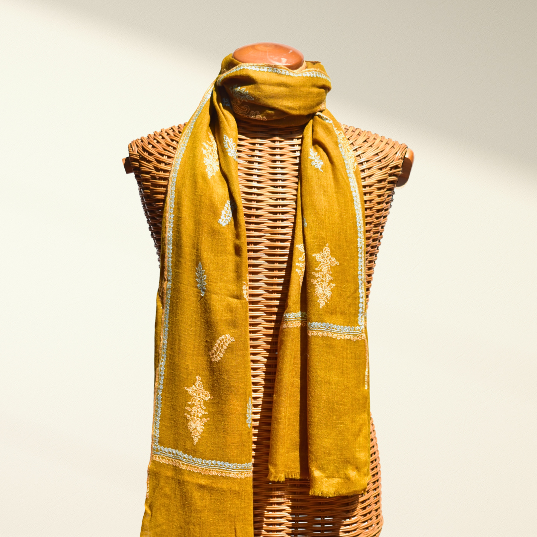 Yellow pashmina stole with patterns draped over a wicker mannequin on a neutral background