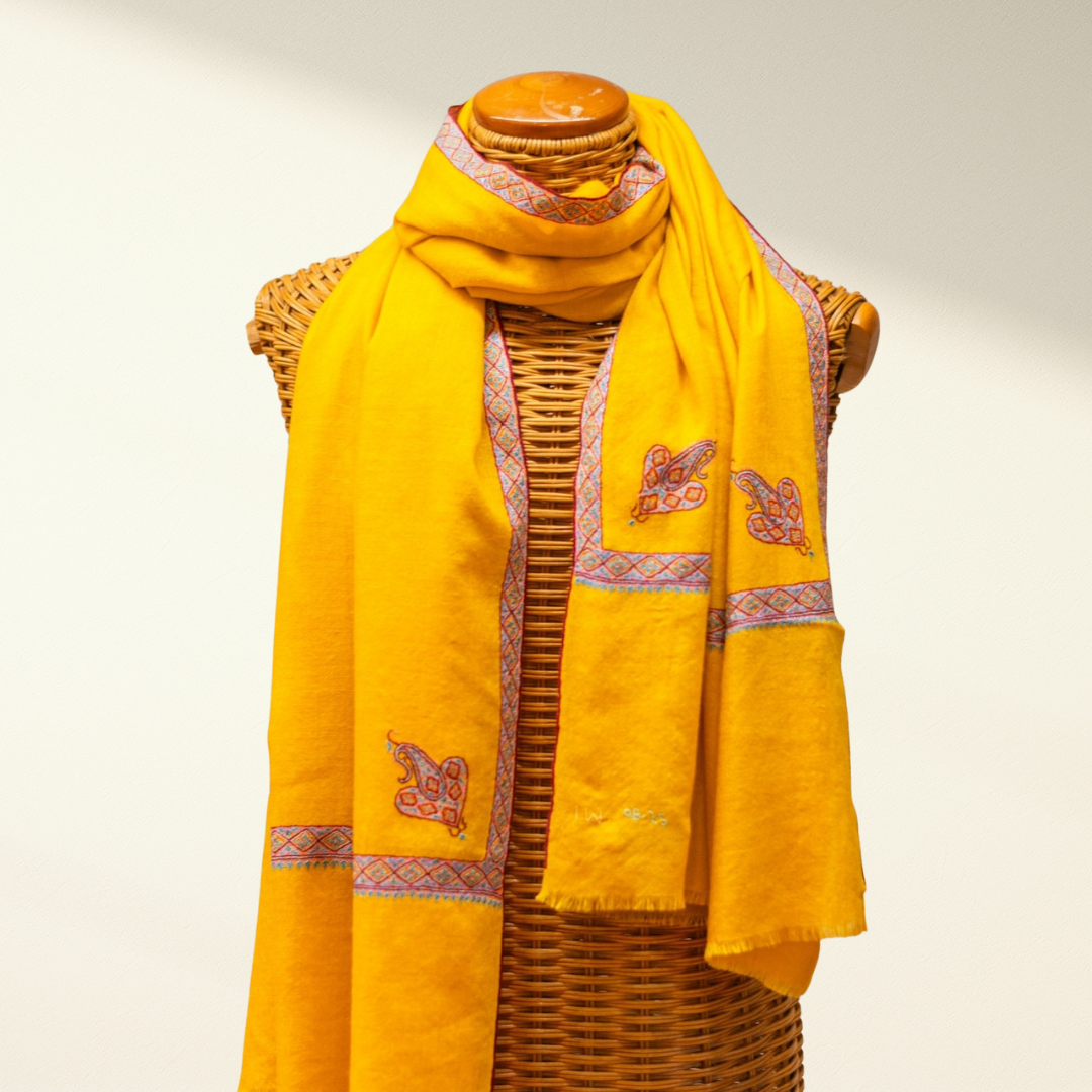 Yellow pashmina scarf with intricate patterns draped over a mannequin against a plain background