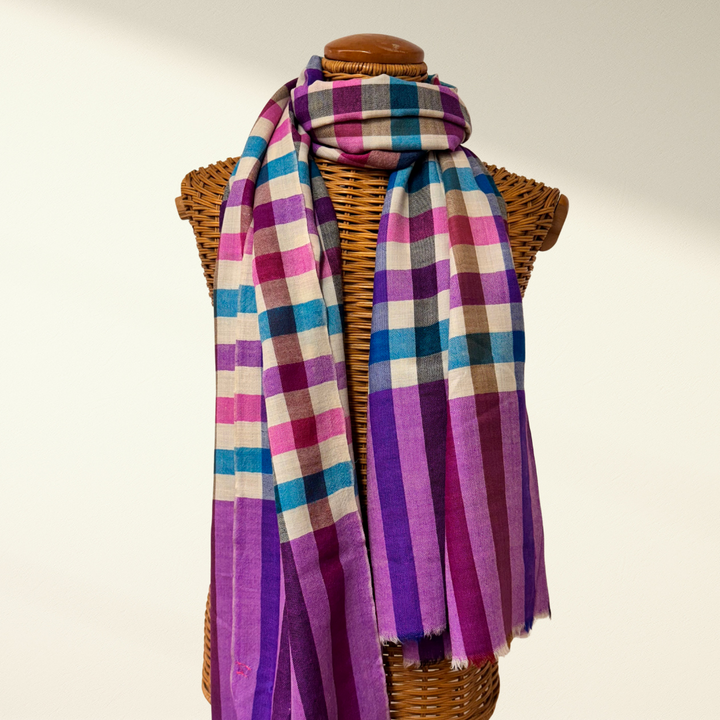 Plaid cashmere scarf with purple and pink tones draped over a wicker basket on a neutral background