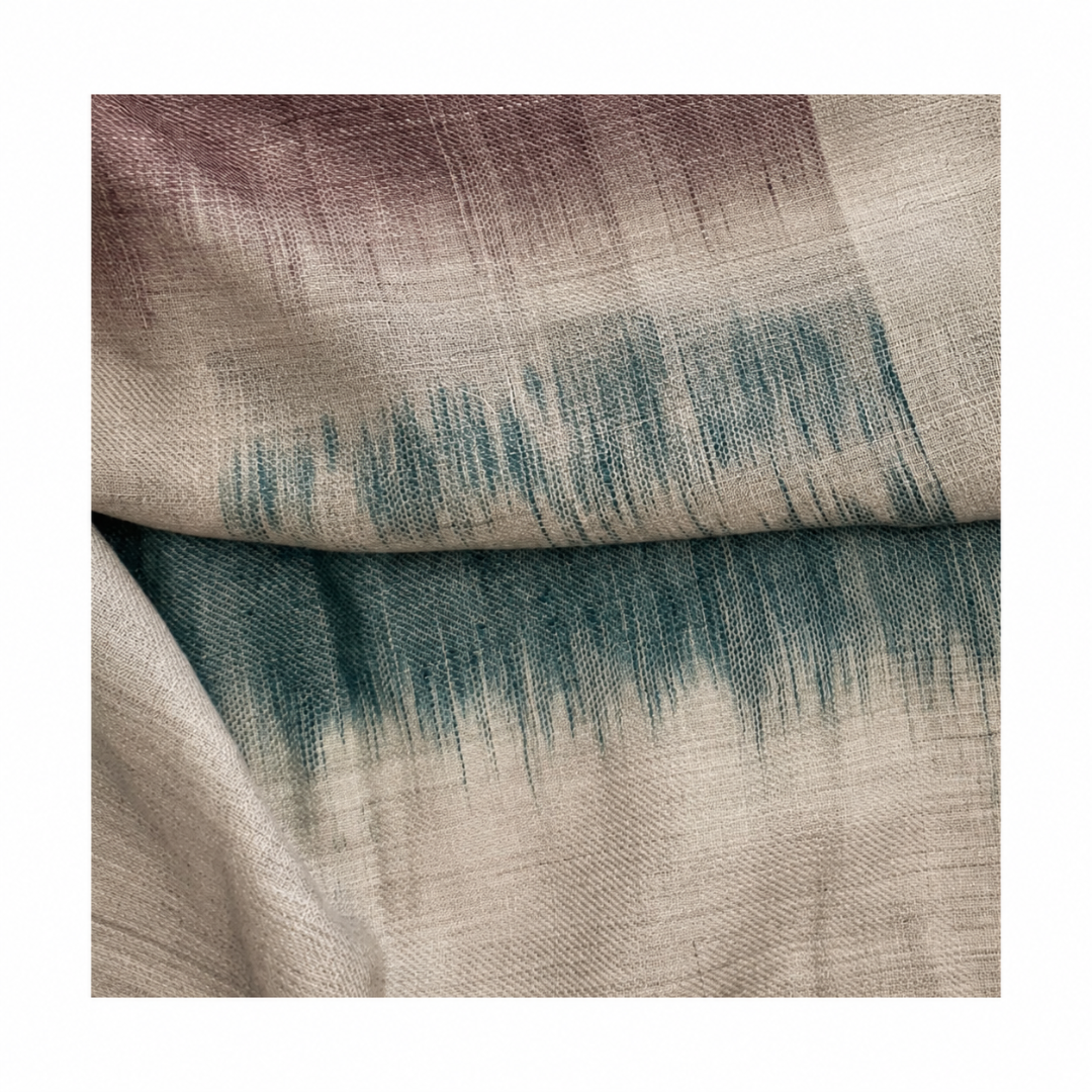 Close-up of a handwoven Pashmina foulard featuring a soft ivory base with muted mauve and deep teal tones, connected through a delicate Ikat-transition that highlights the fine weave and artisanal texture.