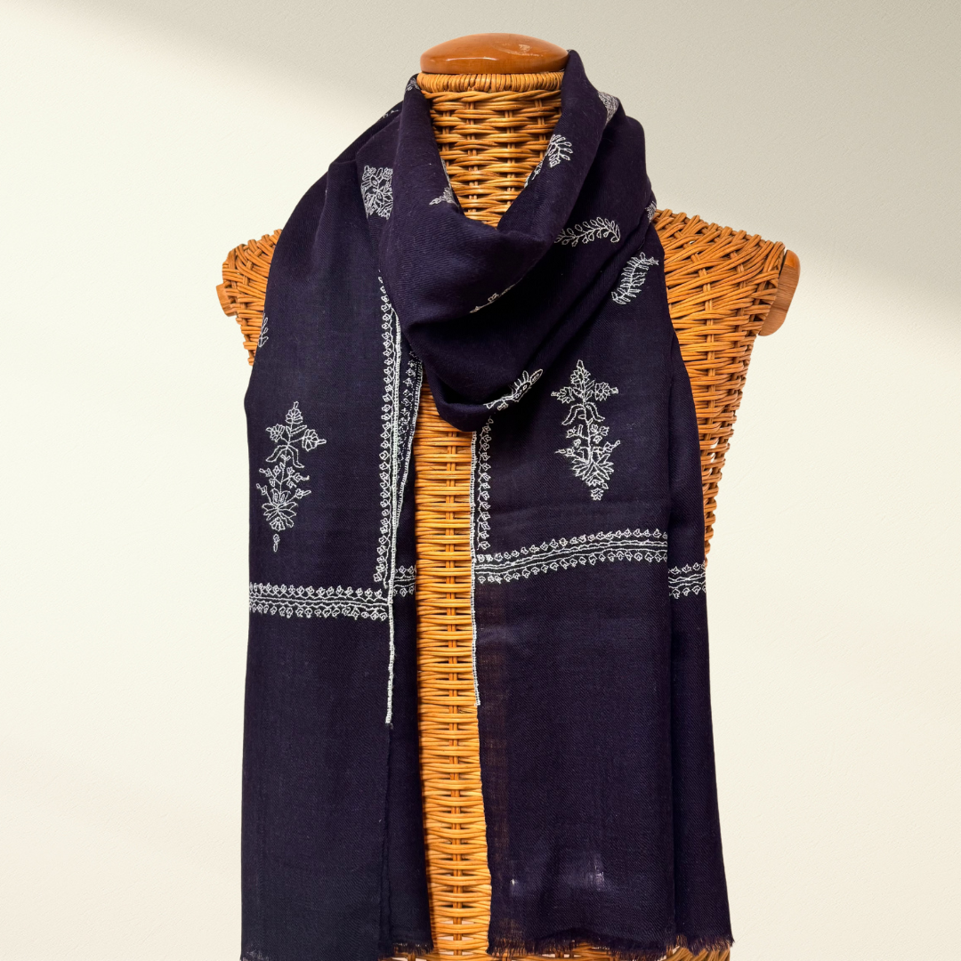 Navy blue pashmina scarf with white patterns draped over a wicker mannequin on a neutral background