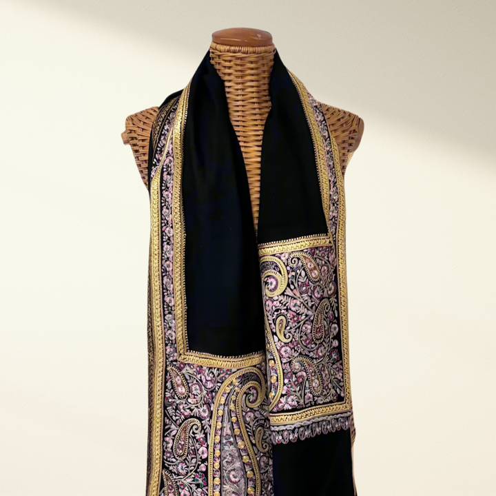 Mannequin wearing a black pashmina shawl with a patterned border on a plain background